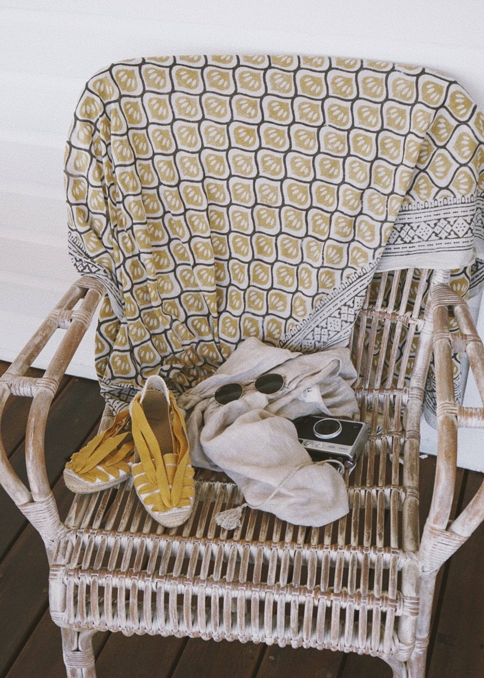 A yellow sarong with a black and cream pattern and black border, displayed on a wicker chair alongside a pair of shoes and other clothing items.